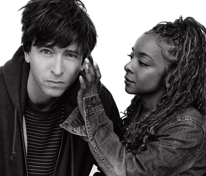 A close-up black-and-white photo of Nicholas Braun and Kara Young with him looking at the camera and her touching his face 