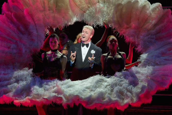 Brian O'Brien as Billy Flynn wearing a tuxedo and singing surrounded by feathered fans