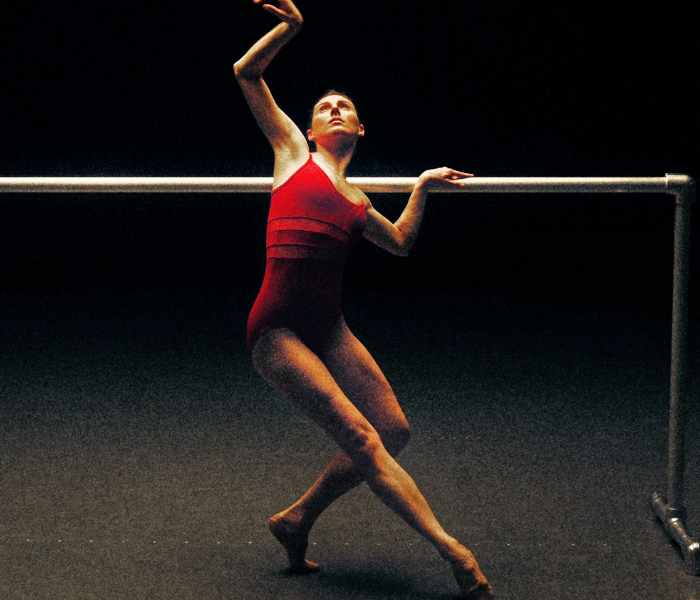 A dancer in a red leotard with her back to the barre warming up