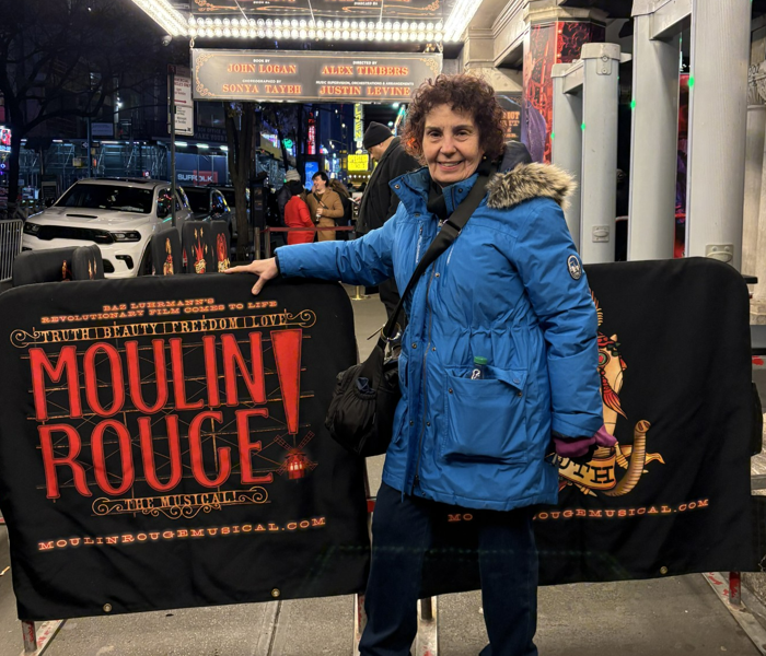 A woman in a blue coat standing by a banner that says Moulin Rouge!