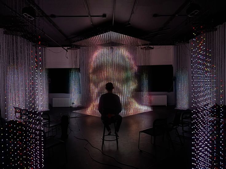 The silhouette of a person sitting in front of an AI rendering of a face