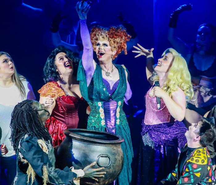 Three actors dressed as the witches from Hocus Pocus in front of a cauldron 