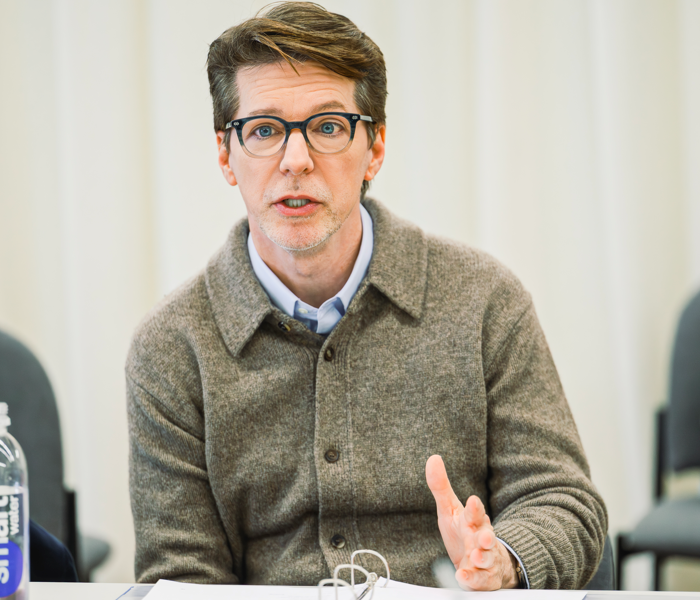 Sean Hayes in rehearsal sitting at a table talking with an intense look