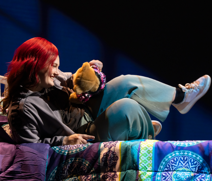 A teenage girl with bright red hair reclining holding a teddy bear