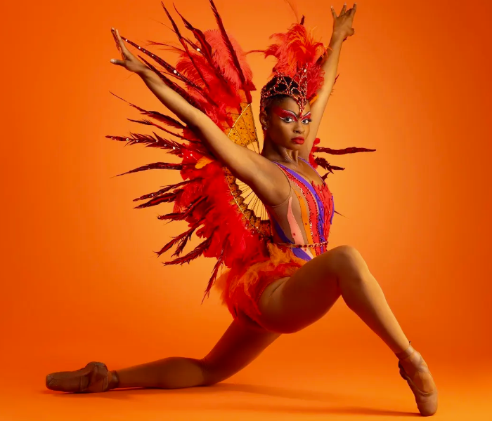 A dancer kneeling in a colorful costume with feathers