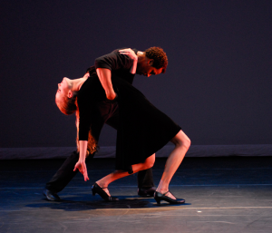 One dancer holding another with her back arched against a black background