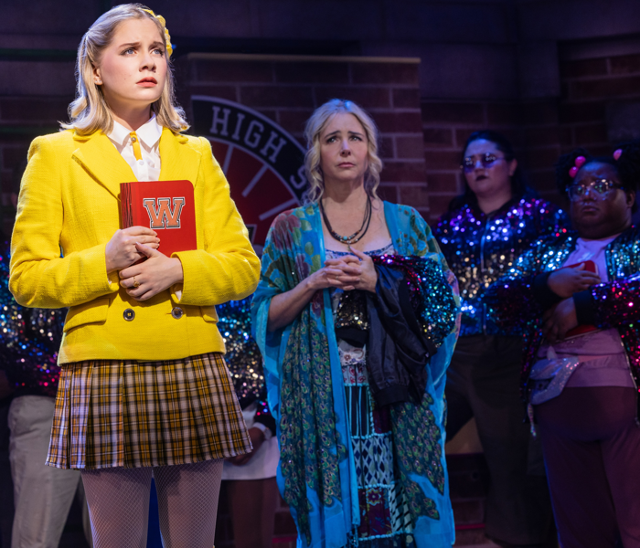 A teen girl in a yellow outfit looking anxious with a woman in blue behind her