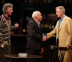Three older men standing in a bar with two shaking hands