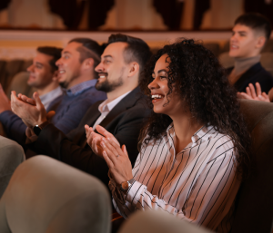 Diverse audience members in a theatre clapping and smiling