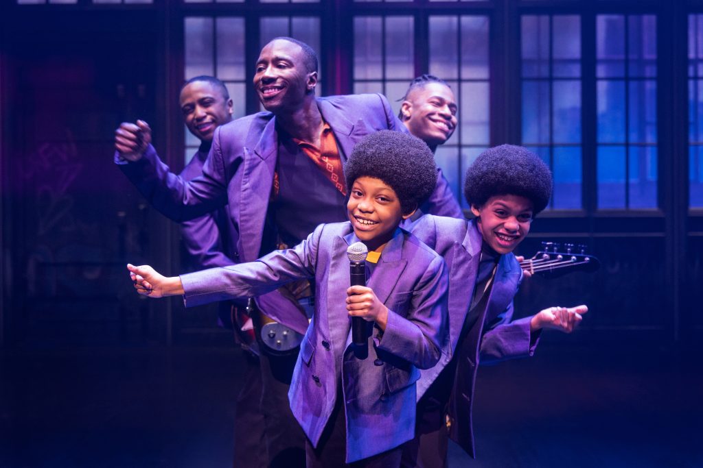 A group of young performers in purple outfits singing