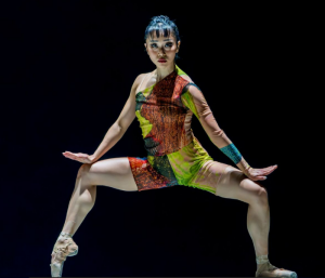 A dancer in a colorful leotard striking a post with her legs askew