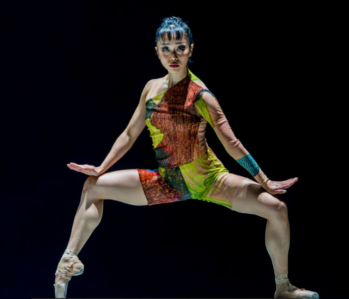A dancer in a colorful leotard striking a post with her legs askew