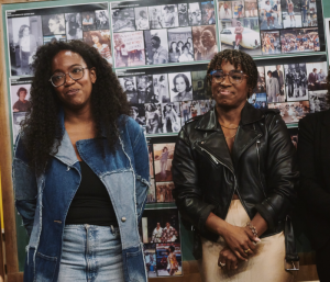 Whitney White and Kristolyn Lloyd standing next to each other smiling in front of a wall of photographs