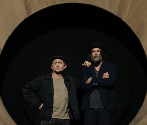 Alex Winter and Keanu Reeves in bowler hats and tattered clothes standing in front of a black circle