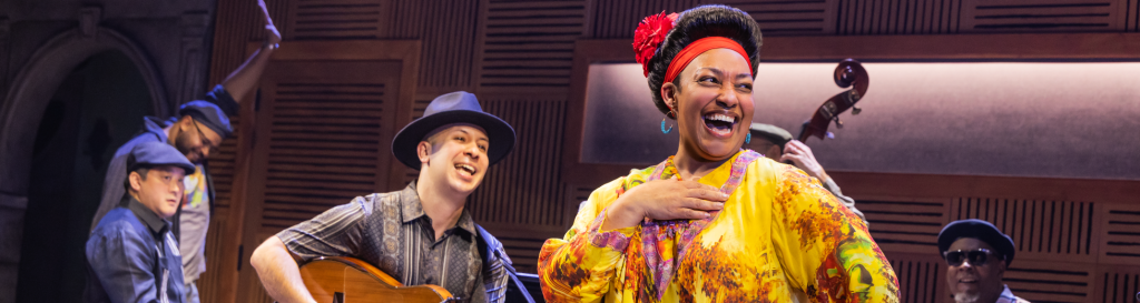 A man playing guitar and a woman in yellow smiling