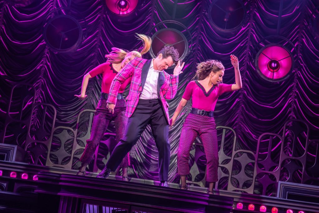 Three performers onstage under pink lights dancing