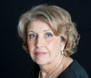 A close-up of Anne Reid looking at the camera with a serious expression