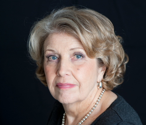 A close-up of Anne Reid looking at the camera with a serious expression