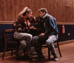 A woman and a man sitting at a table and holding each other's faces