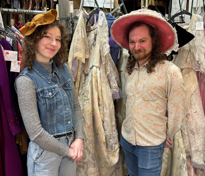 Two people in fancy hats standing next to costume racks