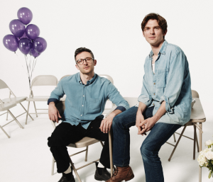 Two men sitting in folder chairs smiling
