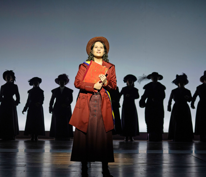 A woman in an orange old-fashioned dress with silhouettes of women behind her