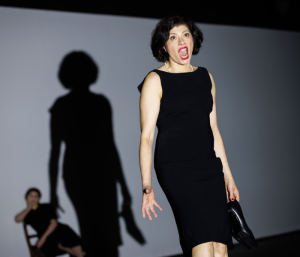 A woman in a black dress looking agitated and singing