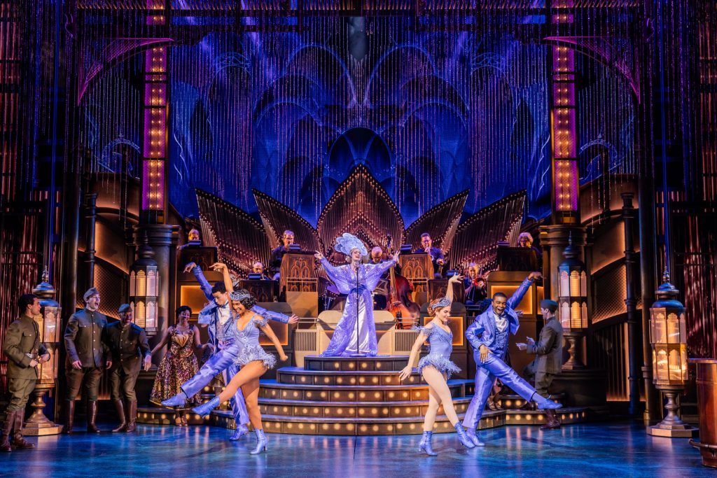 A lavish dance number with three performers in the center in lavender