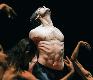 A shirtless dancer arching his back as others writhe around him