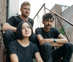 Two men and a woman sitting on stairs outside looking at the camera