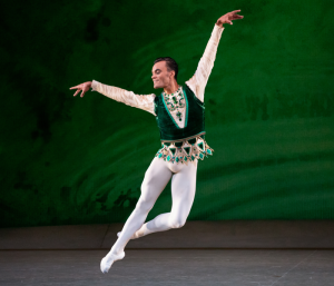 A male ballet dancer leaping against a green background