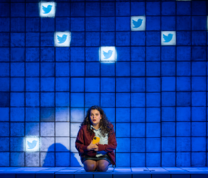 A teenage girl looking worried with Twitter icons projected on the wall behind her
