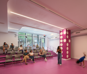 A small theater with pink walls and floor and someone onstage doing a handstand